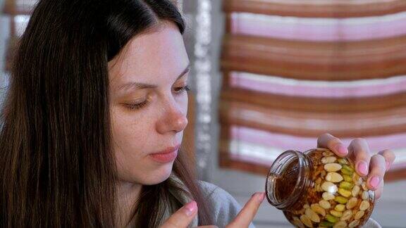 一个女人用手指从一个罐子里拿坚果吃蜂蜜