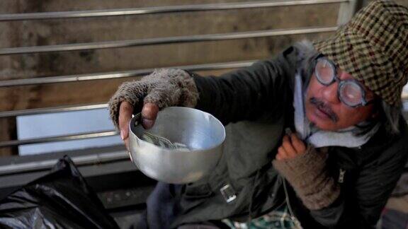 一个无家可归的老人穿着脏衣服坐在街上寻求帮助