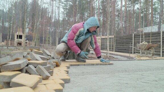 一个建筑工人正在用黄色的铺路石建造人行道