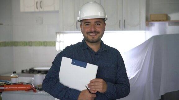 拉丁美洲的承包商在一个房屋项目中改造厨房在剪贴板上做笔记然后对着镜头微笑
