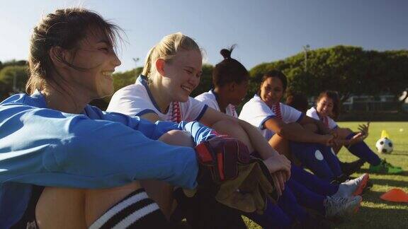 快乐的女足球运动员坐在足球场上聊天4k