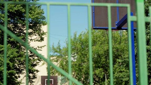 在围栏后面的慢动作镜头两个年轻的女运动员一起打篮球在室外城市球场女孩成功射门进篮网得分