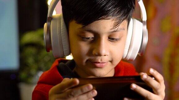 男孩戴着耳机在智能手机上玩游戏的照片