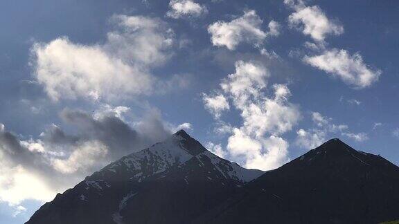 在格鲁吉亚高加索地区日落时白云在白雪皑皑的山顶上飘过蓝天