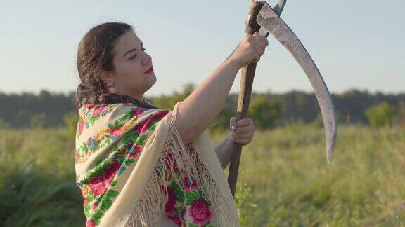 肖像的美丽超重的女人磨镰刀准备开始在绿色的夏天的田野上割草