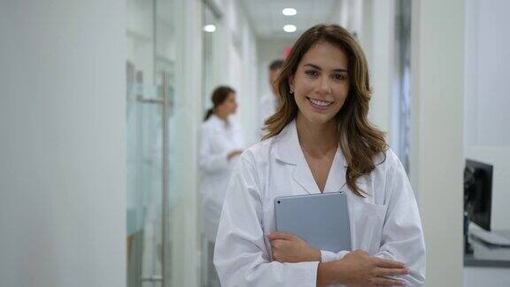 拉丁美洲女医生在医院工作拿着数码平板电脑看着相机微笑