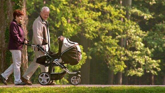 爷爷奶奶在公园里和他们的孙子在婴儿车里散步