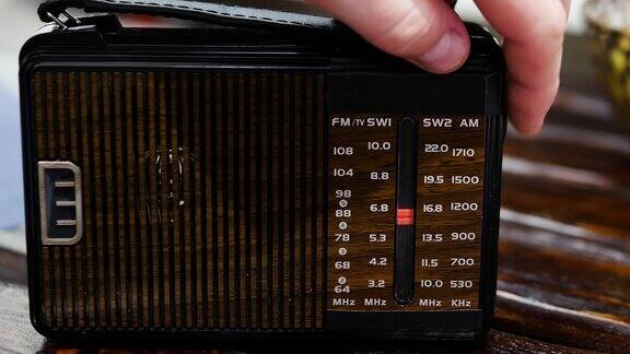 一名男子在一张旧木桌上用收音机收听无线电波带天线的古董接收机把模拟收音机调到一个音阶上一个男人在用一台旧收音机听新闻听音乐