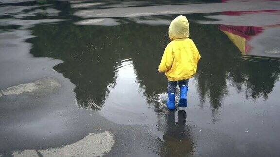 小男孩在户外散步在水坑上跳跃