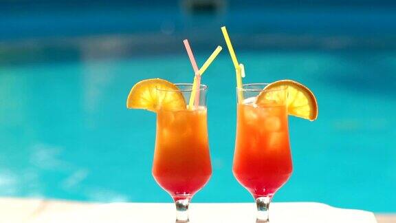 两杯橙色鸡尾酒在泳池的背景上