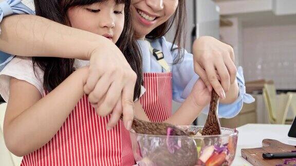 4k慢镜头年轻的亚洲母亲和女儿快乐和乐趣准备蔬菜沙拉在一个现代的白色厨房女儿做饭时心情愉快