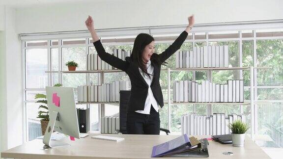 穿着黑色套装的快乐商务女性在电脑屏幕前工作在办公室里跳舞休息