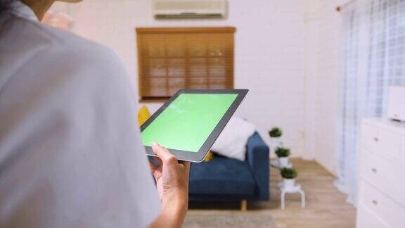 女人用绿屏平板电脑应用来控制家里客厅的空调智能家居自动化控制概念