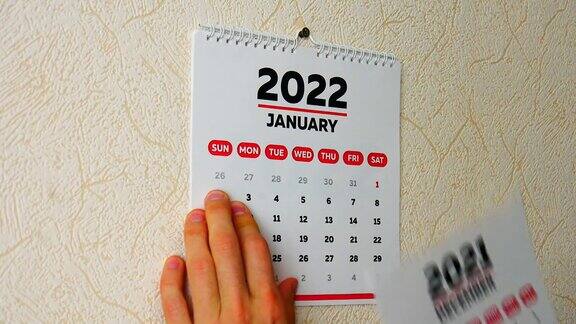 一名男子用手撕下挂在墙上的2021年日历的12月页然后撕下2022年新日历的1月页