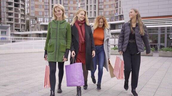 四个漂亮的女朋友走在街上愉快地聊天四个时尚女性拿着购物袋