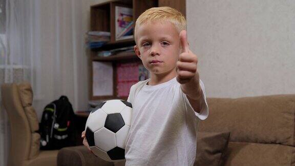 一个小男孩在家里手里拿着一个足球竖起大拇指