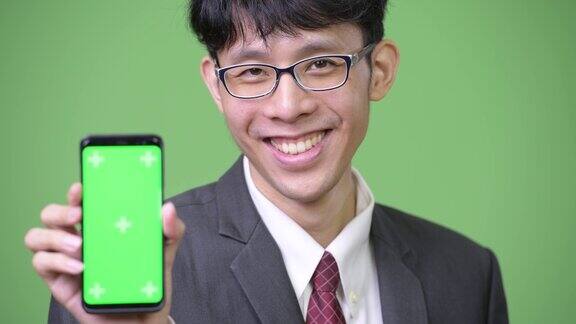 年轻快乐的亚洲商人微笑着向镜头展示手机