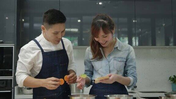 年轻的亚洲妻子和丈夫一起在厨房跳舞和努力做饭