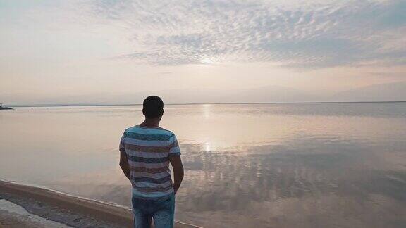 一个年轻人站在死海的岸边欣赏美丽的日出美丽的海景黎明