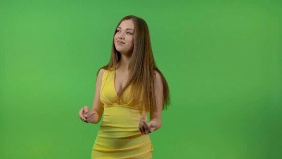 绿色屏幕上穿着黄色裙子的漂亮女孩她转过身来做了个手势