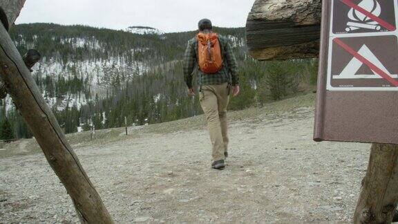 一名年轻的白人男子背着背包走过“禁止营火”和“禁止露营”的标志在科罗拉多州的落基山脉在一个阴天的冬天徒步旅行