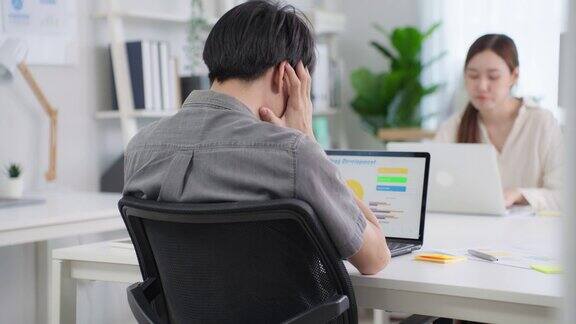 沮丧的亚洲商人工人在办公室工作场所的桌子上工作在公司的笔记本电脑桌上忙碌的员工们会因为加班和加班而感到疲惫和头痛