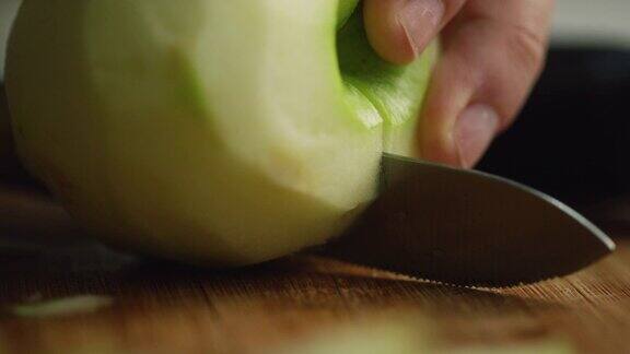 一个女人的手切一个削了皮的苹果在一个木制砧板上用菜刀切成两半的极端特写镜头