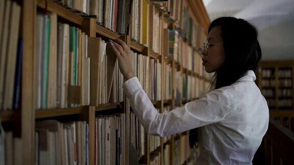 穿着白衬衫的年轻亚洲生物学家学生从书架上拿旧书