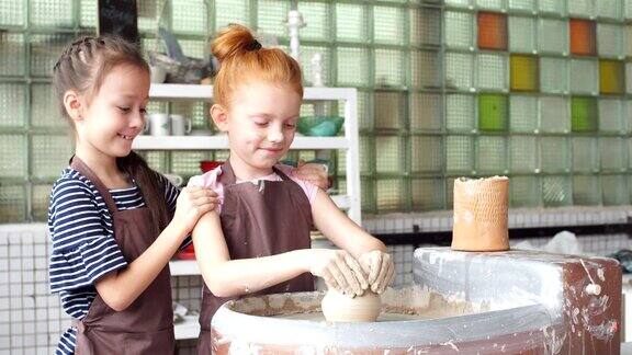 两个小女孩在一个陶轮上玩粘土玩得很开心