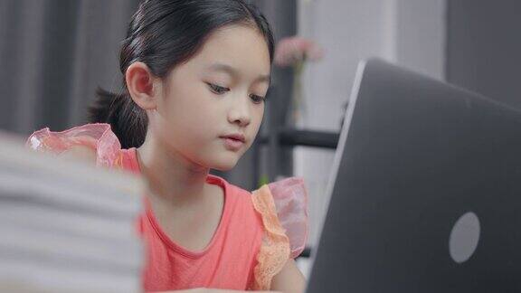 迷人的亚洲小女孩在冠状病毒或新冠病毒封锁的情况下在笔记本电脑屏幕上和老师一起学习电子学习和在线家庭学校她有视频电话技术和她的建议学习她的家庭作业