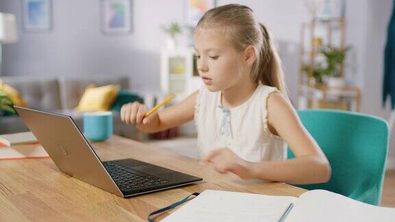 聪明的小女孩在客厅里做家庭作业她坐在书桌前用笔记本电脑用钢笔在课本上写字