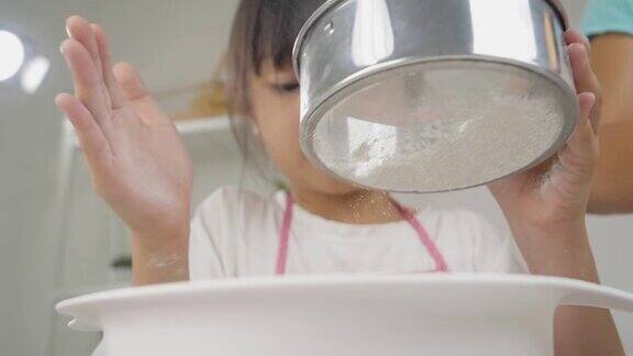 快乐的亚洲孩子在家里学习做饼干女孩筛面粉到搅拌碗