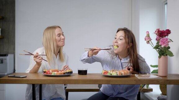 两个可爱的年轻女孩吃寿司卷和聊天朋友一起在厨房
