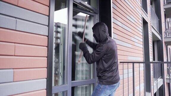 小偷从院子或阳台溜进公寓一个穿着黑色夹克、戴着面具的男人透过玻璃门往房间里看
