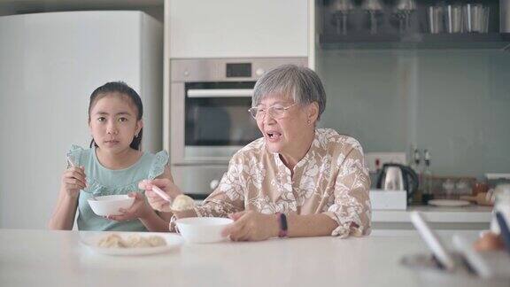 亚洲华裔孙女和她的祖母在厨房的柜台吃饺子