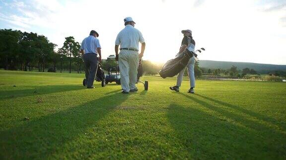 在夏日夕阳下亚洲商人和高级CEO一起拿着高尔夫球袋漫步在高尔夫球道上