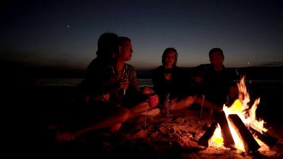 朋友们坐在篝火旁的沙滩上两对情侣在一起玩吉他玩得很开心