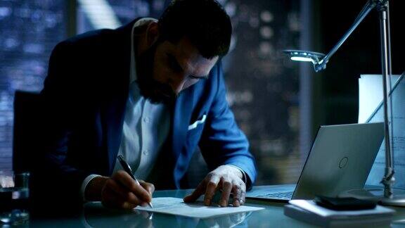 深夜商人在他的私人办公室里用笔记本电脑签署文件可以看到大城市的窗户