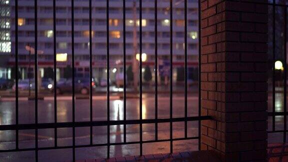 雨夜潮湿的城市街道透过金属栅栏的夜间交通画面