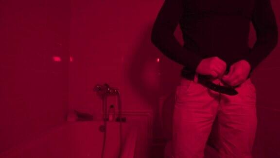 上完厕所后穿裤子的年轻人红色灯光下的洗手间一个男人在夜总会的厕所里