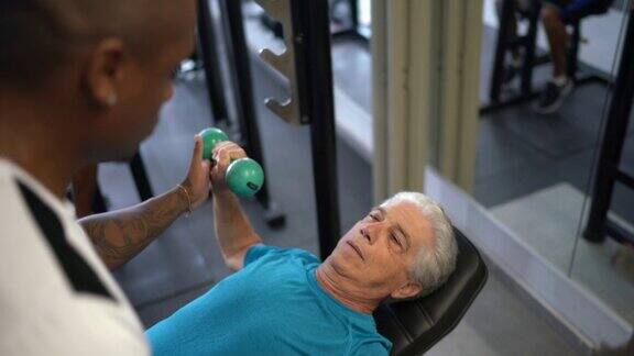 一位老人在他的私人教练的帮助下在健身房锻炼