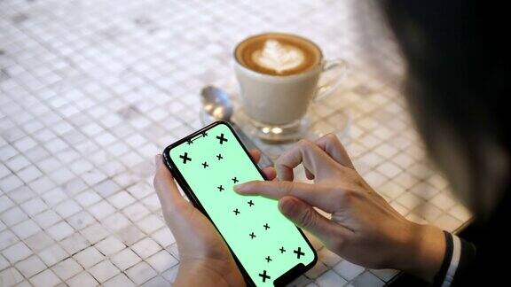 一名女性在咖啡馆使用绿色屏幕的智能手机