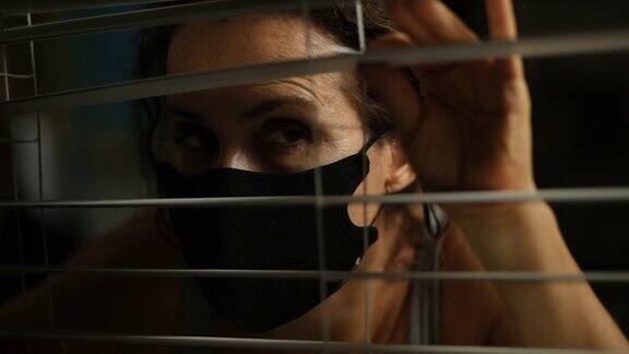 害怕的成熟女人在晚上戴着防护面具透过窗户偷看