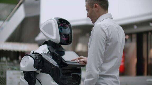 一名身穿衬衫的男子与一个白色机器人交流机器人问问题并用手指按屏幕