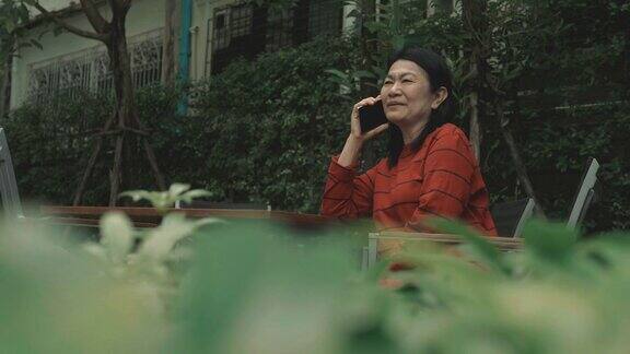 年老的亚洲妇女正在用电话在阳台与树