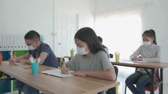 一群亚洲小学生戴上卫生口罩在教室里防止Covid-19的爆发返校时重新开学教育理
