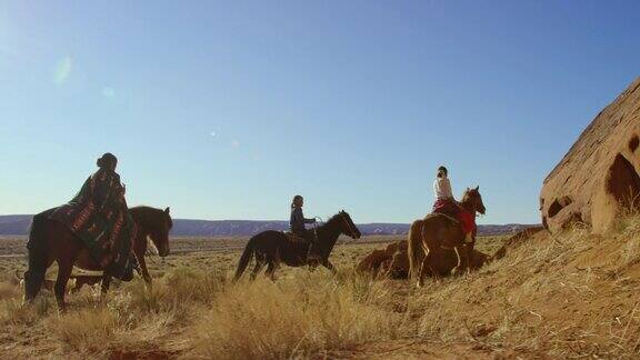 几个年轻的美国原住民(纳瓦霍)儿童骑马穿过纪念碑谷沙漠在亚利桑那州犹他州旁边的一个大的岩石形成在一个晴朗明亮的日子