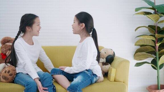 两个上小学的亚洲女孩坐在家里的沙发上一起唱歌多年龄段的孩子或女性朋友们穿着白色t恤在上课前一起唱歌兴奋地开始学习快乐的时间