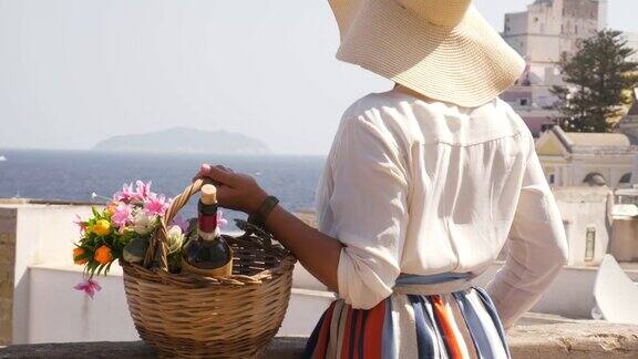 年轻女子拿着花篮看着海边的庞扎镇岛意大利时尚色彩艳丽的裙子和大礼帽典型的城市