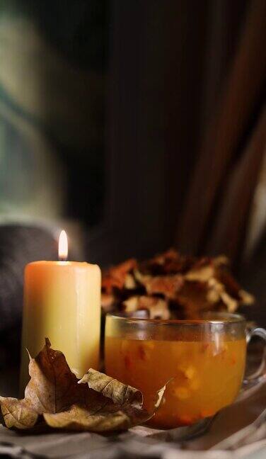 女手搅拌热橙沙棘茶在一个舒适的家秋天傍晚静物与干燥的叶子